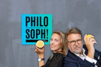 Podcast „Philosoph!“ mit Martin Gräfer und Anna Kuhns: Zwei Personen vor grauer Wand halten Zitronen in der Hand.